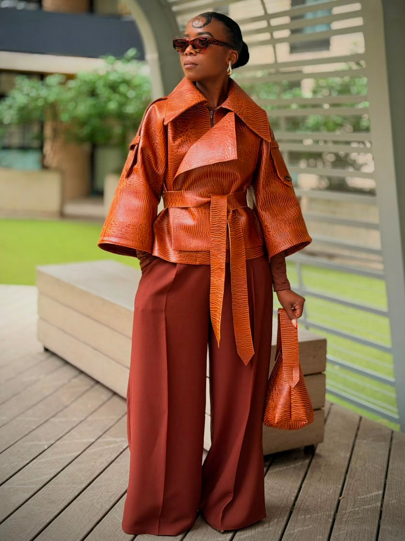 Woman standing in a cognac textured faux leather jacket with a wide collar and belt