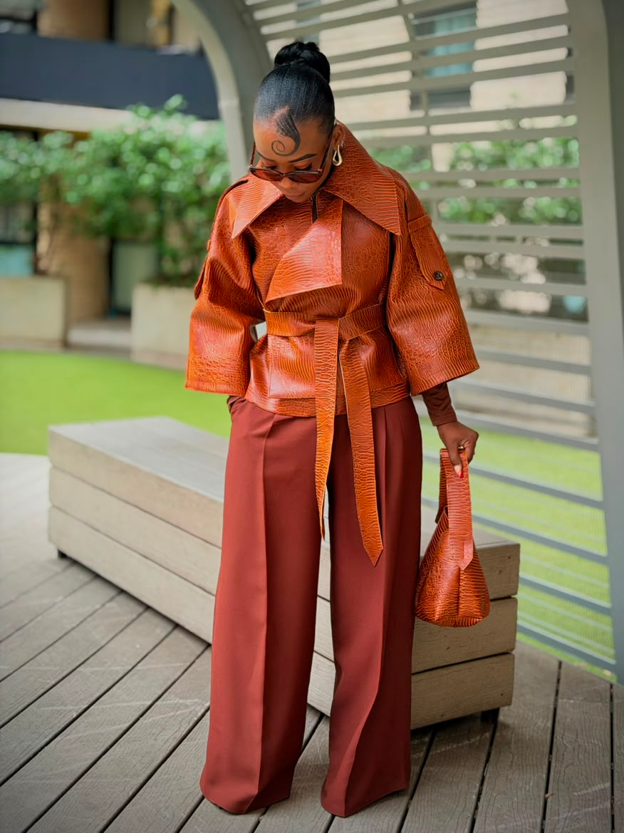 Woman standing in a cognac textured faux leather jacket with a wide collar and belt