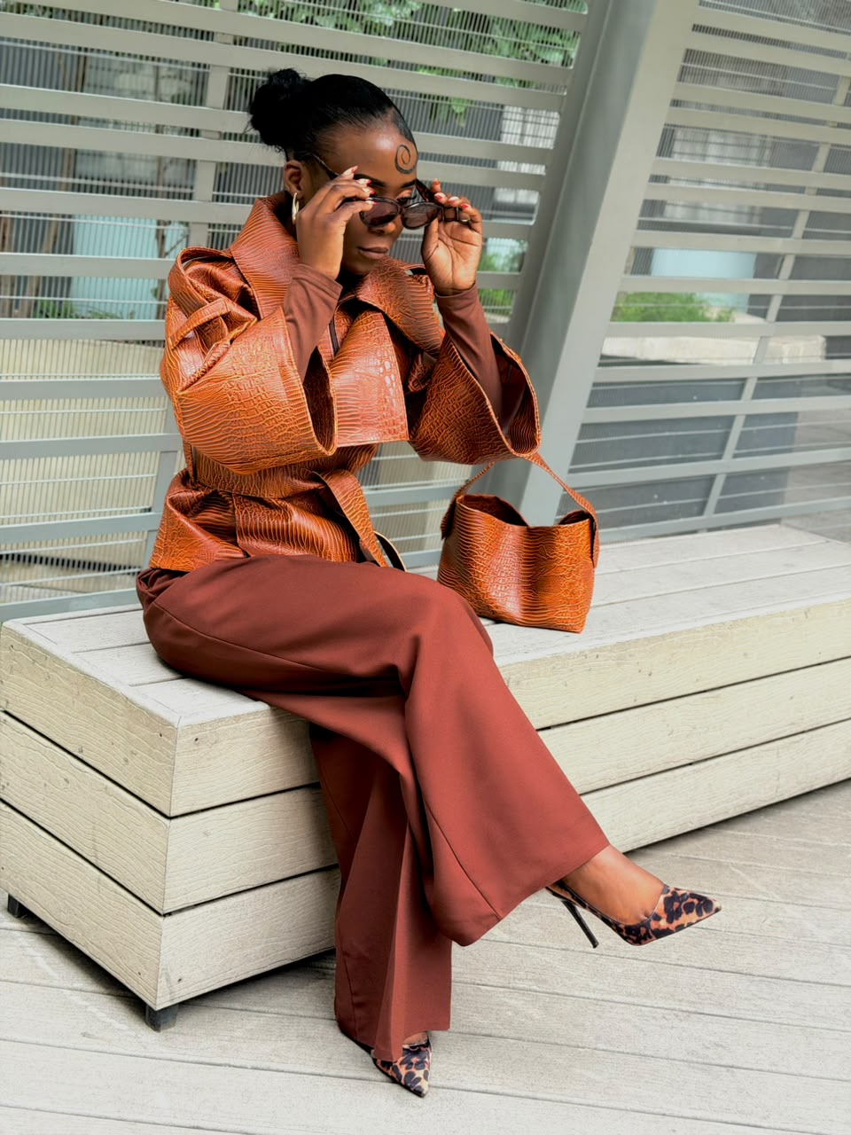 Woman wearing a cognac textured faux leather jacket with wide-leg trousers, seated
