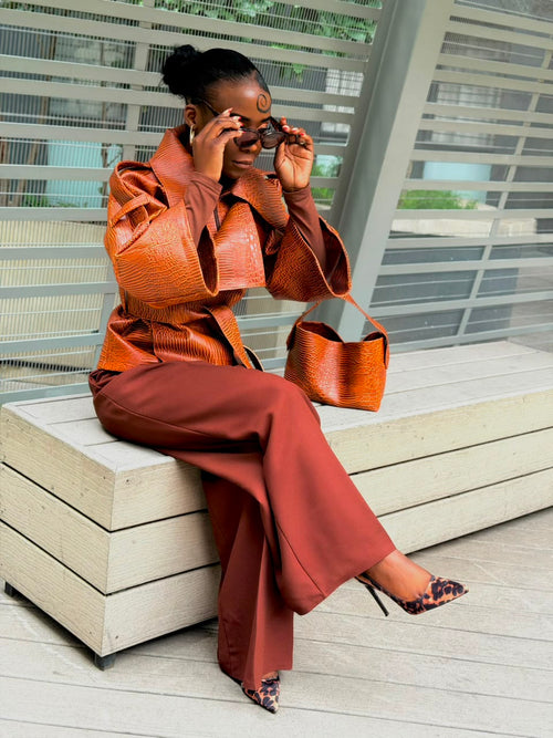 Woman wearing a cognac textured faux leather jacket with wide-leg trousers, seated