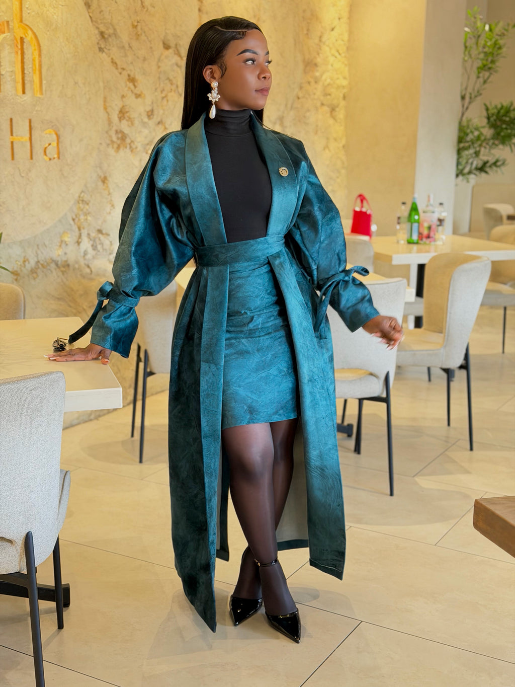 Teal textured long belted coat and matching mini skirt, worn with black tights and heels