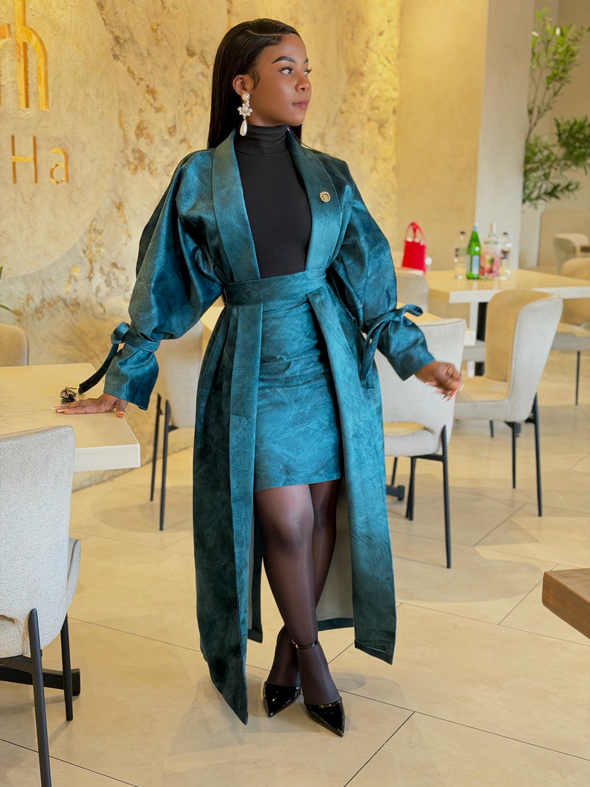 Teal textured long belted coat and matching mini skirt, worn with black tights and heels